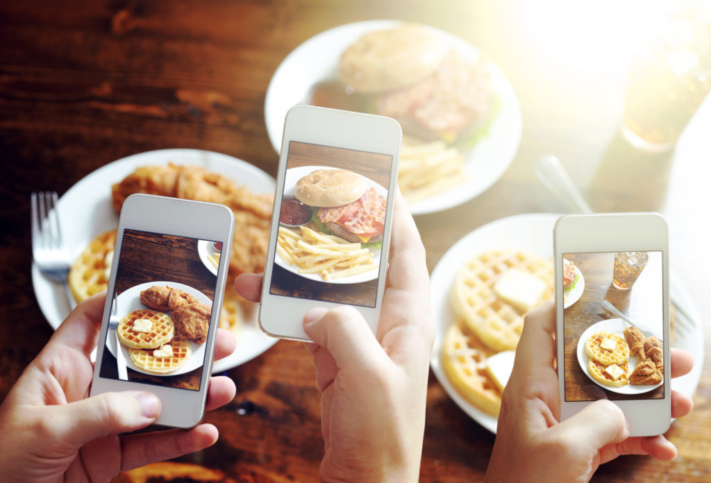 friends using smartphones to take photos of food with instagram style filter at restaurant