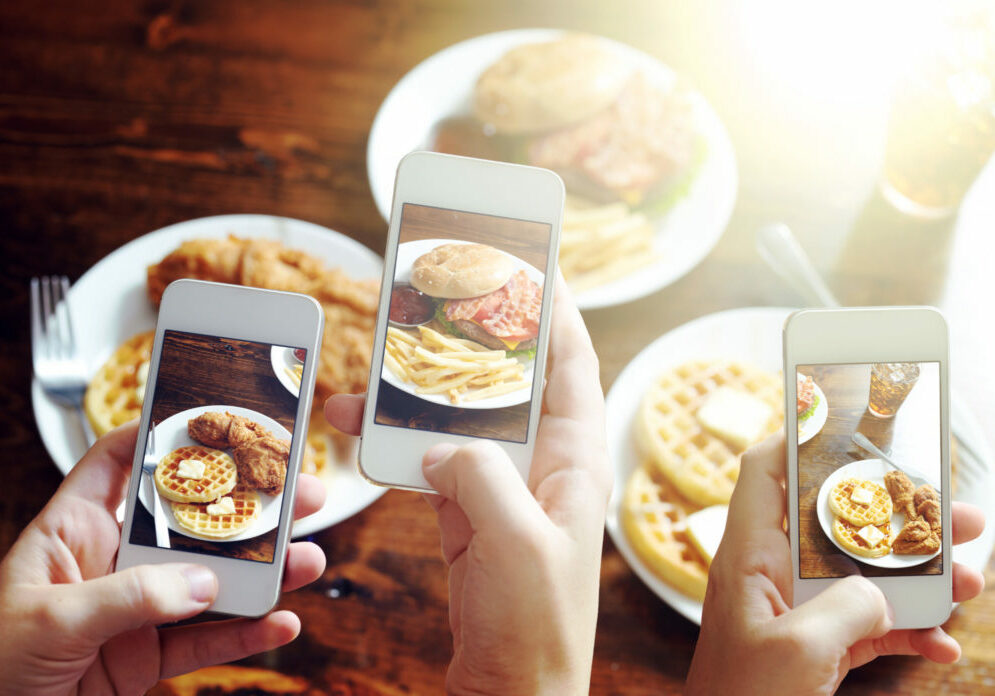 friends using smartphones to take photos of food with instagram style filter at restaurant